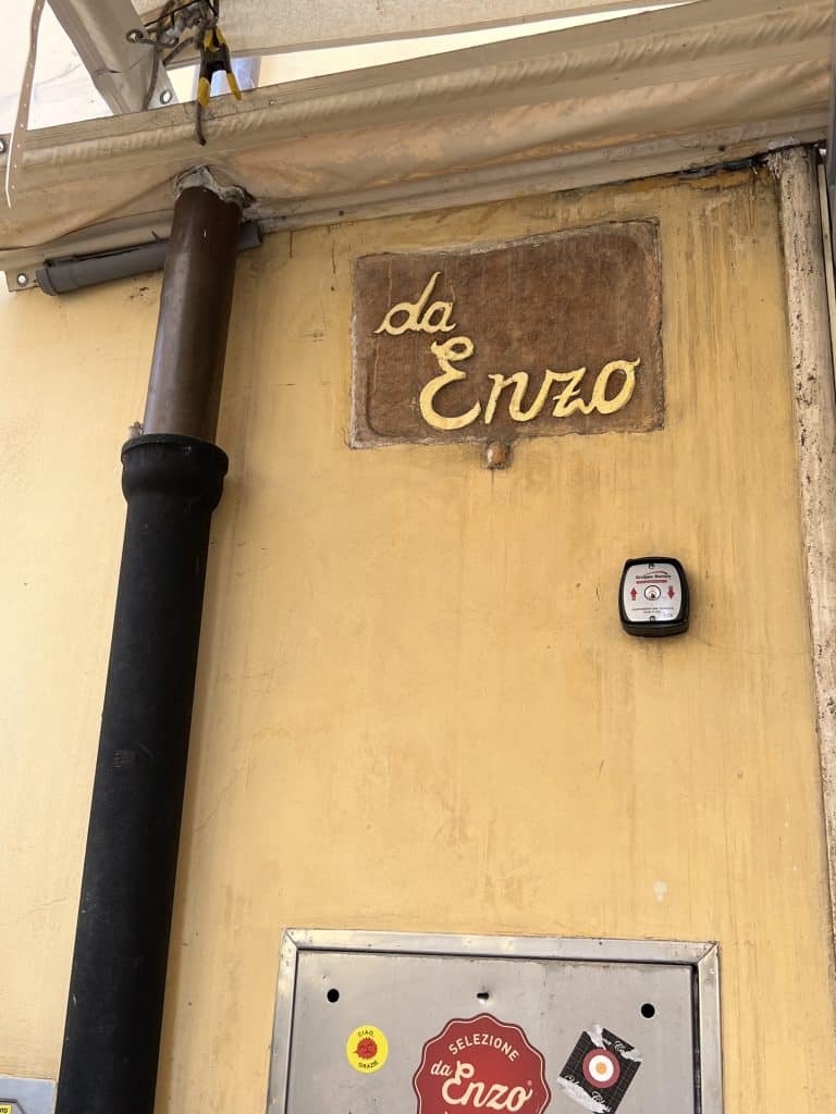 Brown sign of the restaurant Da Enzo on a yellow wall.