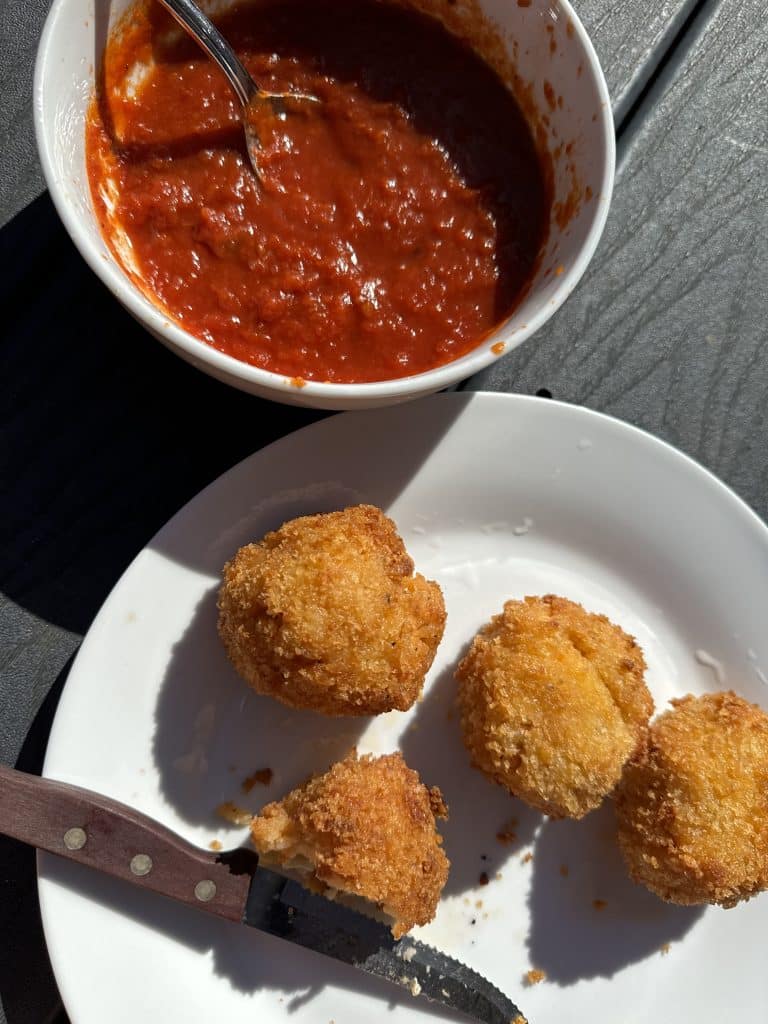 Homemade suppli in a white plate next to a bowl of tomato sauce.