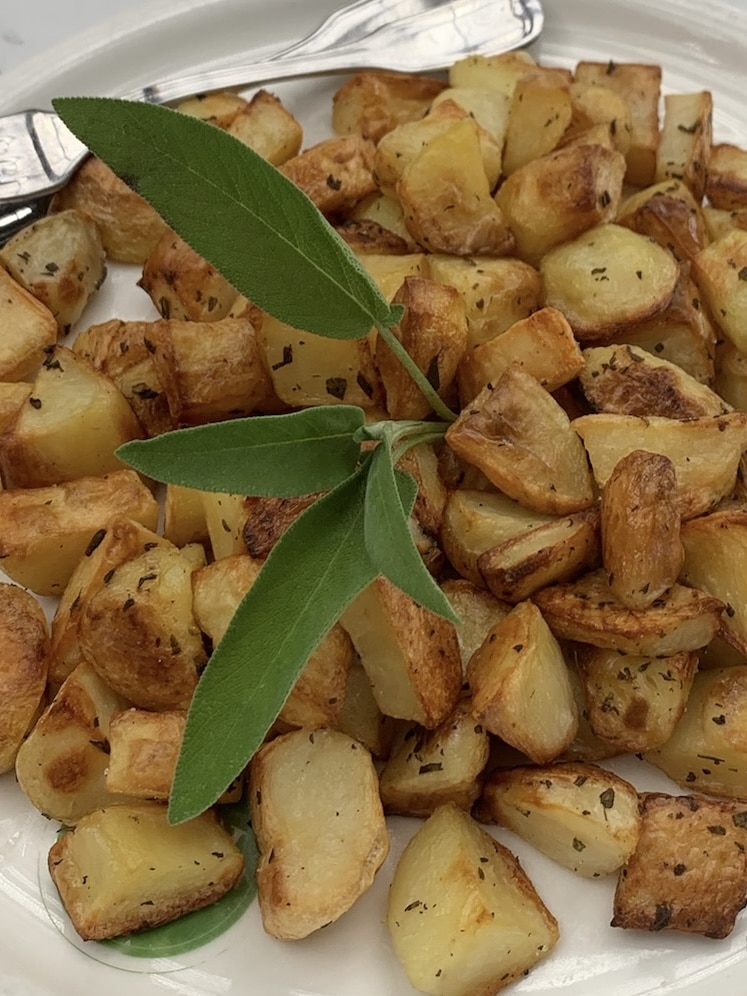 Plate of roasted potatoes with sage and rosemary.