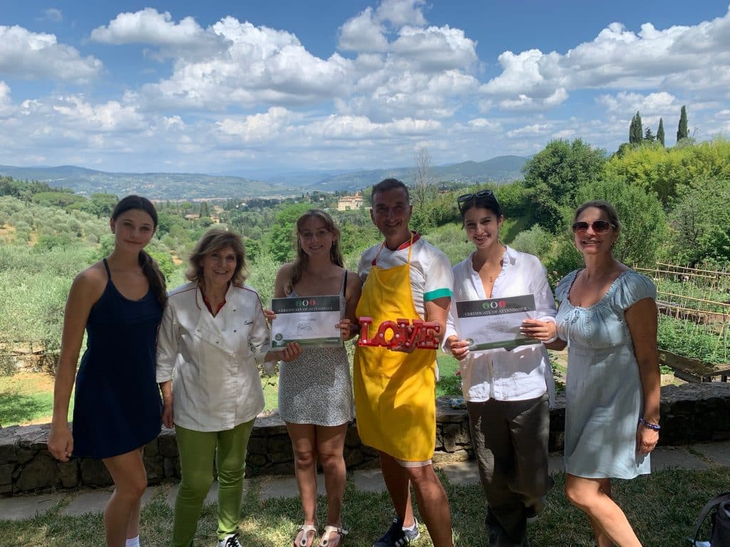 A family receiving cooking class certificates with the chefs in front of a Tuscan countryside landscape.