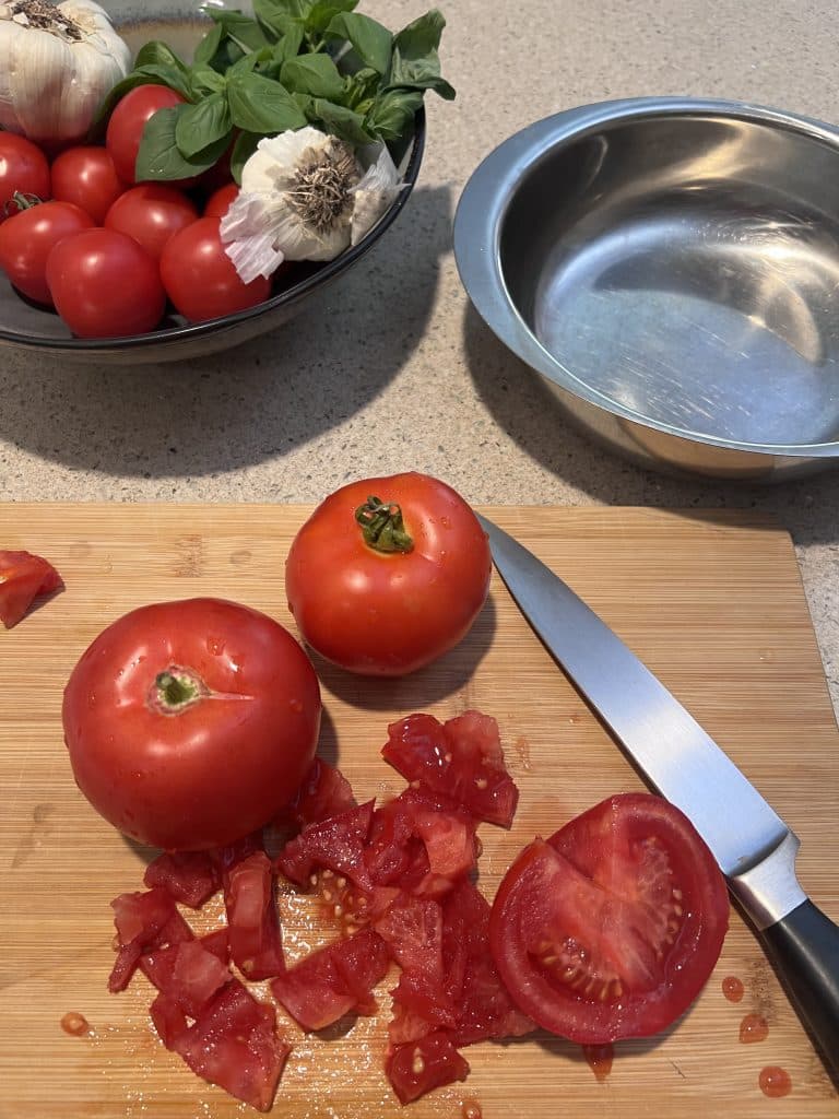 Whole and diced tomatoes on a cutting board with knife.