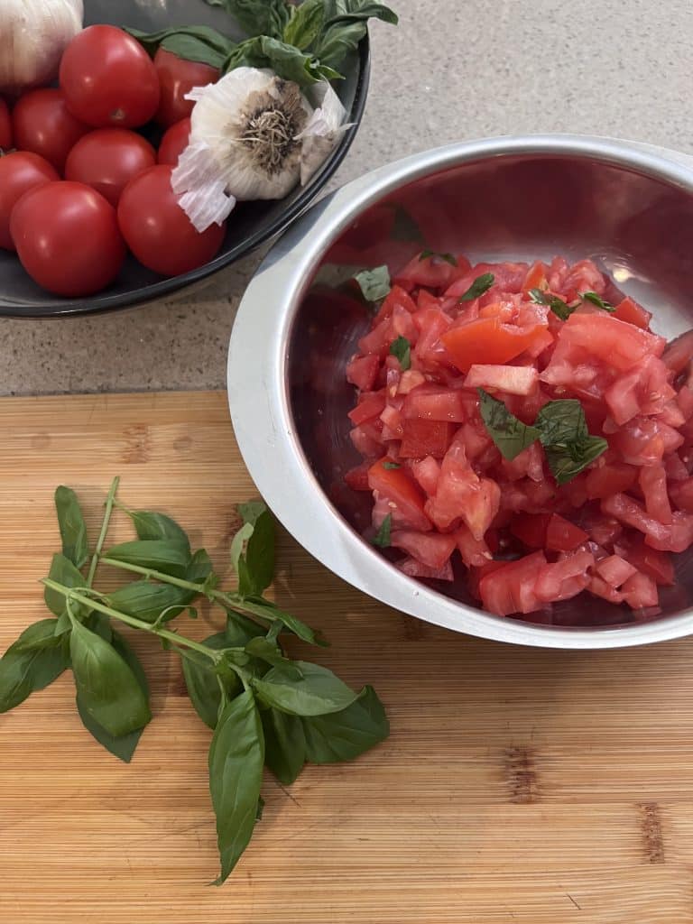 Basil on cutting board next to bowl of diced tomatoes