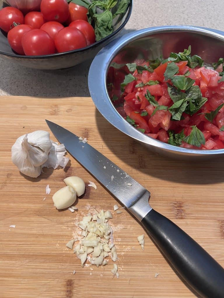 Chopped garlic on cutting board with knife.