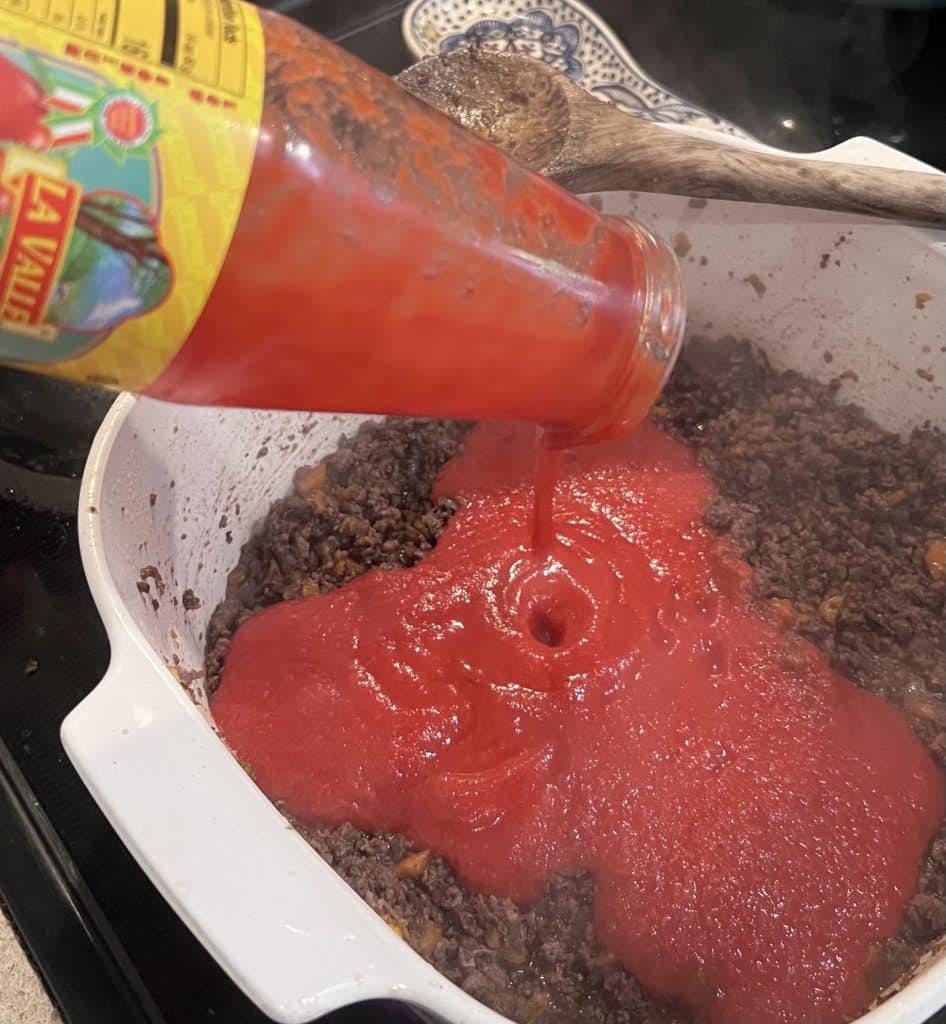 Adding tomato passata to the browned meat mixture.