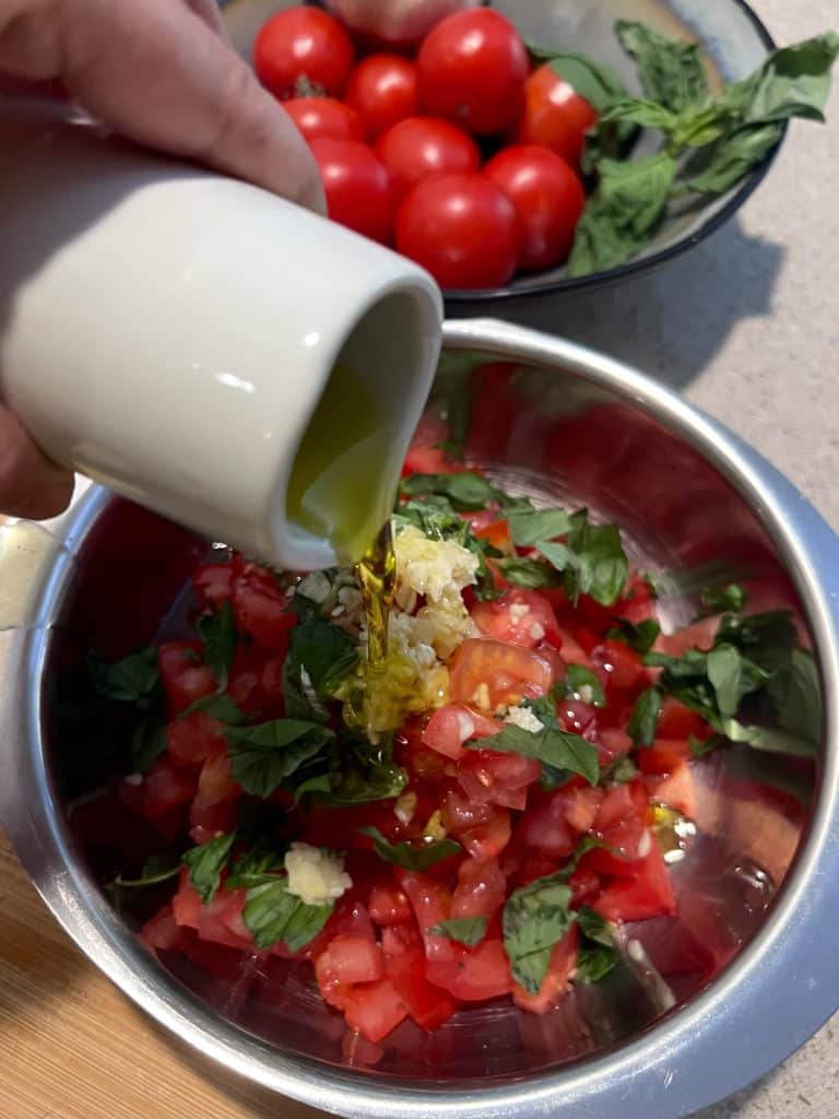 Olive oil being poured over tomato, basil, and garlic mixture.