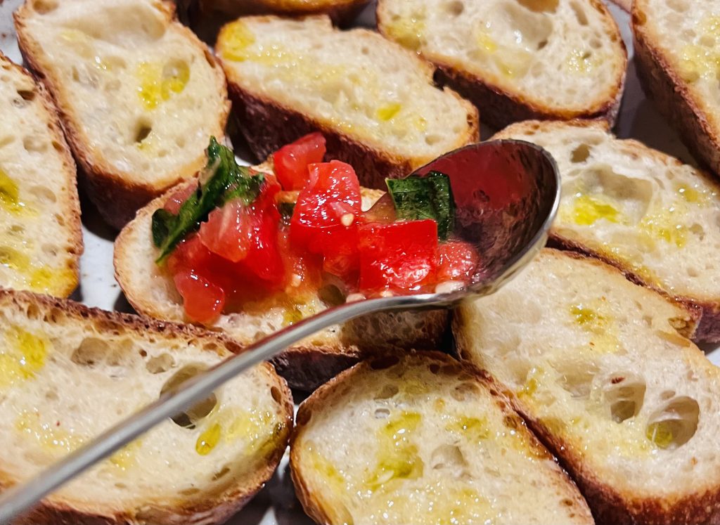 Spoon with tomato topping on top of bruschetta.