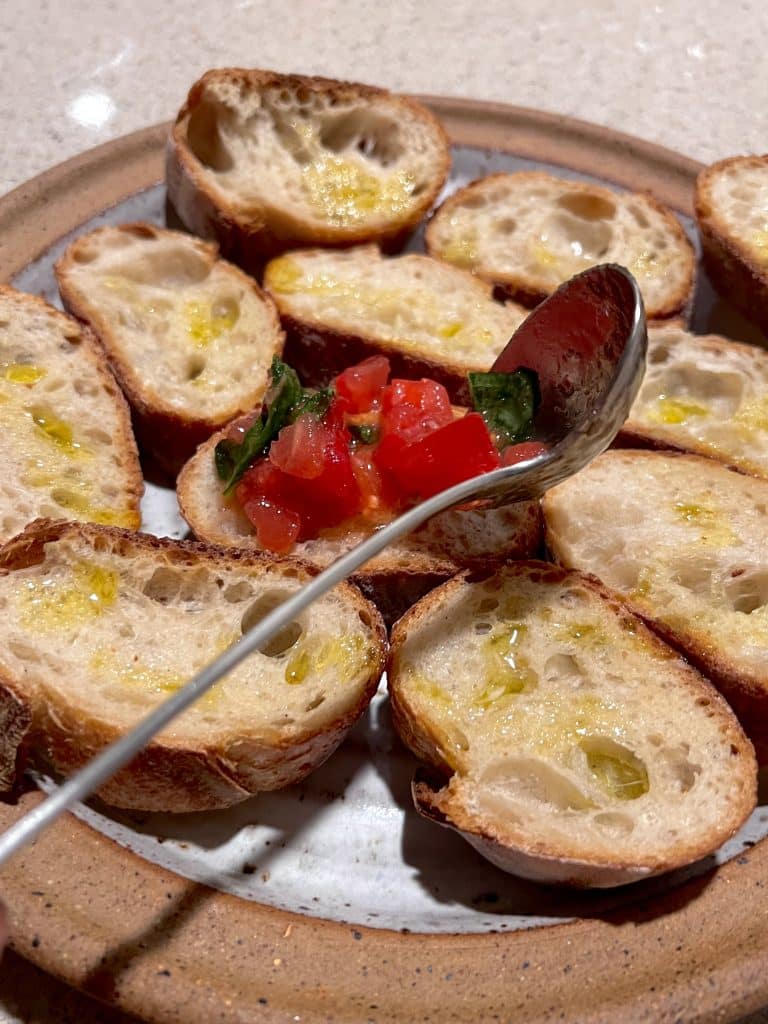 Plate of oven toasted rustic bread with a spoon of tomato tuscan bruschetta on top.