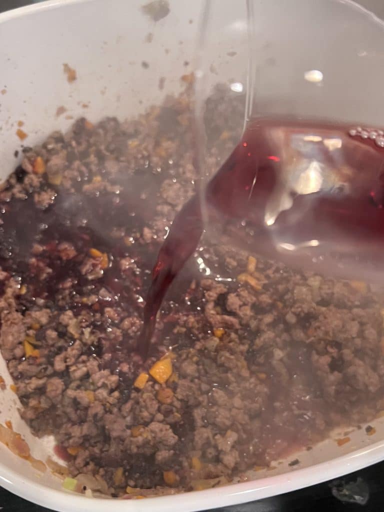 Adding red wine to the browned meat and soffrito