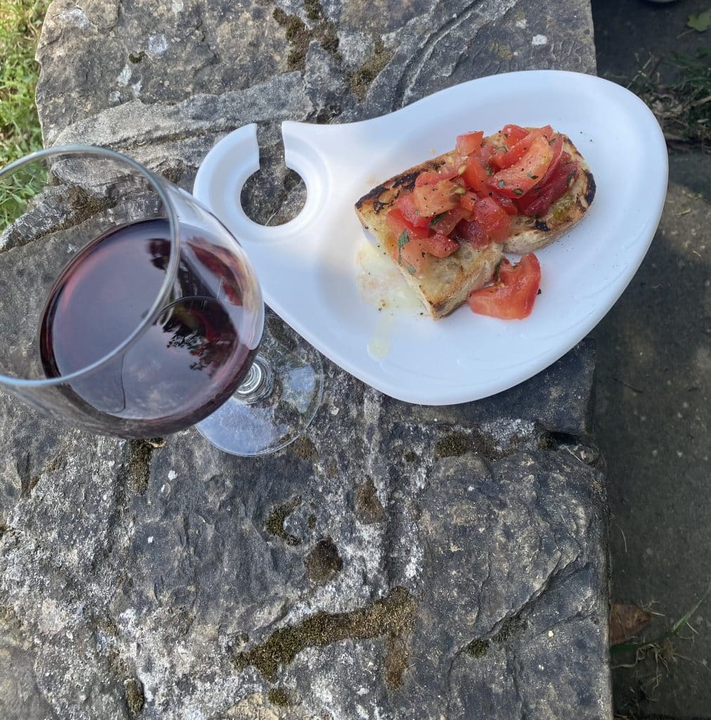 Bruschetta on a white plate that has a cut out to hold a wine glass. Glass of red Chianti Classico.