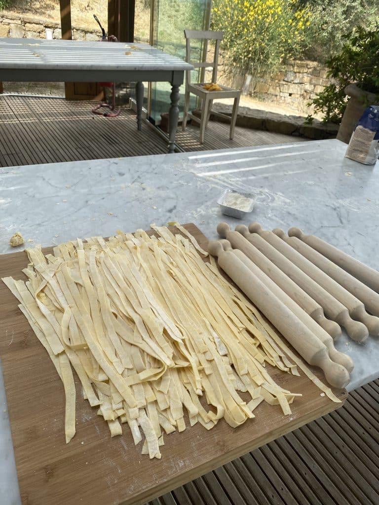 Freshly made tagliatelle laid out on the cutting board and 7 rolling pins on a marble table top.