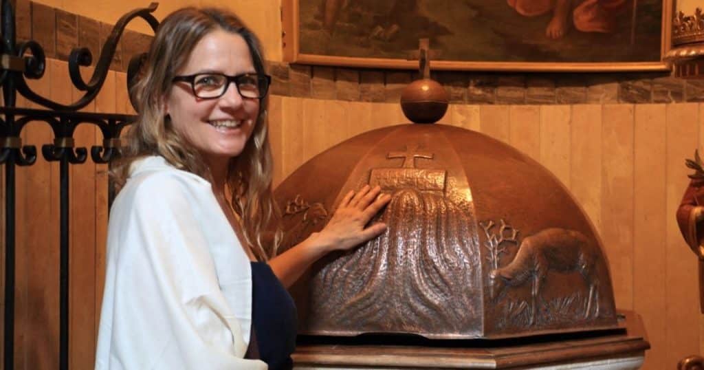 Woman touching a baptismal font. Ancestry tours in Italy are deeply personal.