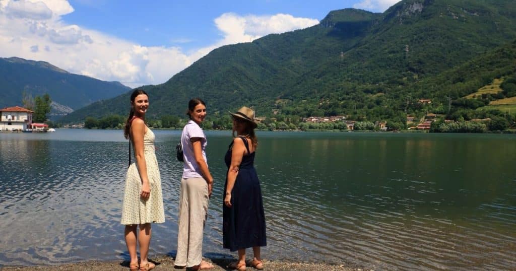 Three women at the edge of a lake surrounded by steep green hills. Ancestry tours in Italy are immersive.