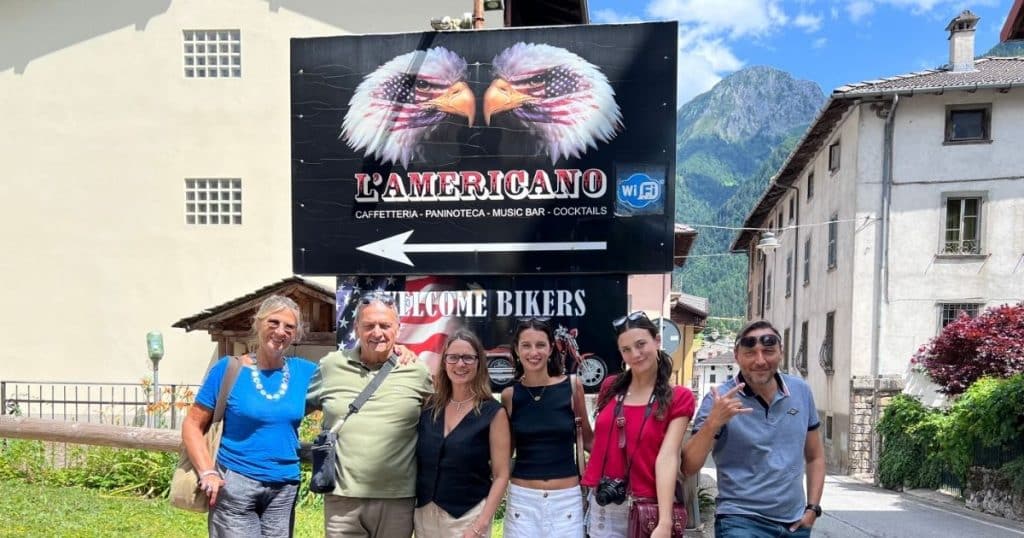 Group of people in front of the Americano sign in Schilpario with mountains in the background. We met our cousins during this  ancestry tour in italy.