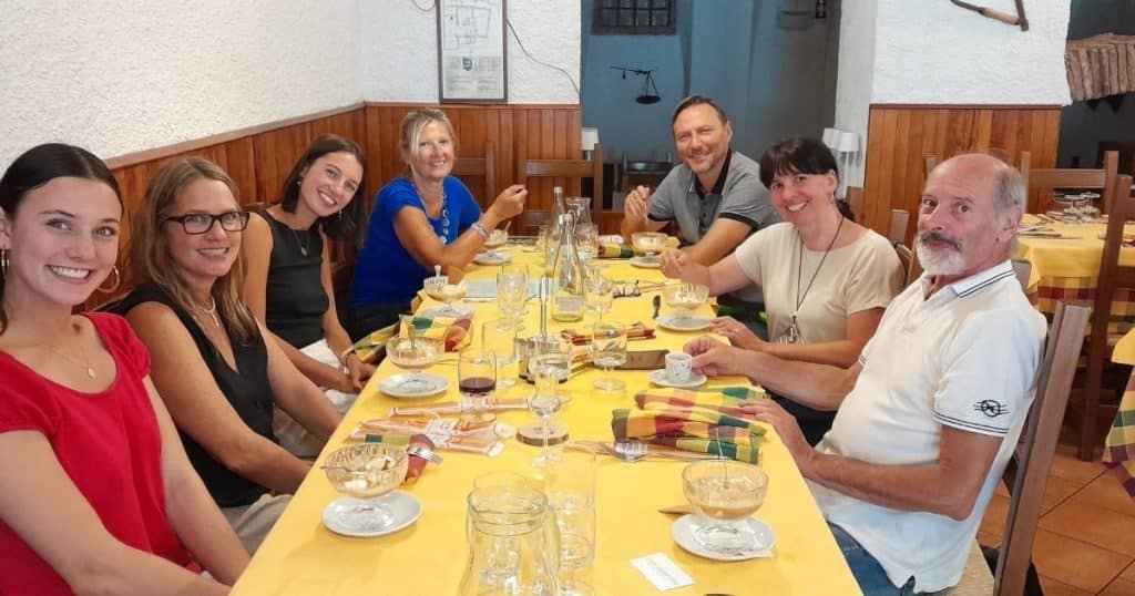 Group of people having lunch at a long table with yellow table cloth in a restaurant in Schilpario. Ancestry tours help with making lasting connections.