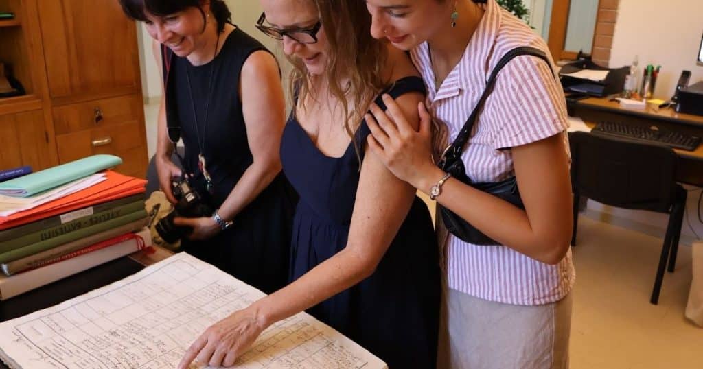 Three women looking down at ancestor records in a parish book. Ancestry tours in Italy include a personal tour with a genealogist.