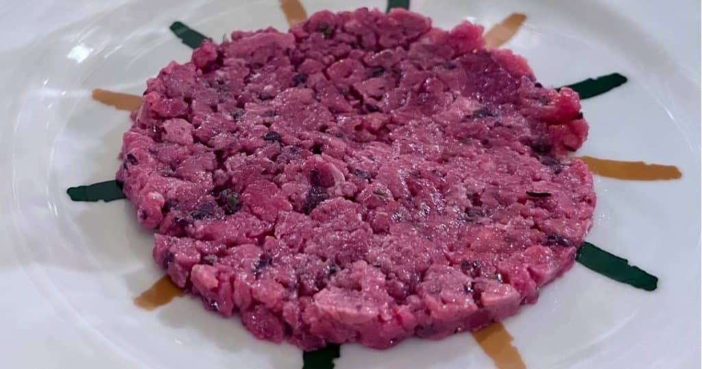 Finely chopped beef tartare plated in a round shape with a sunburst pattern of sauce and herb garnish at Il Mannarino