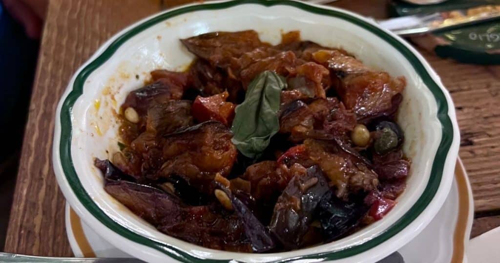 Eggplant caponata with pine nuts, olives, and fresh basil in a green-rimmed bowl at Il Mannarino