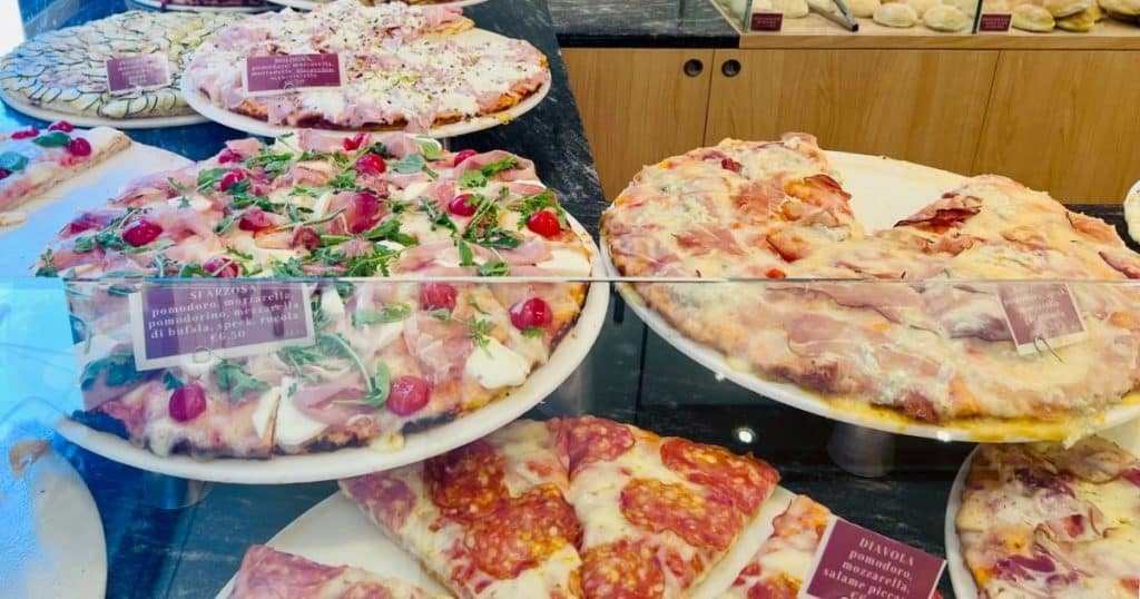 Display case of pizza al trancio varieties at il Forno, including Sfarzosa with prosciutto and arugula, and Diavola