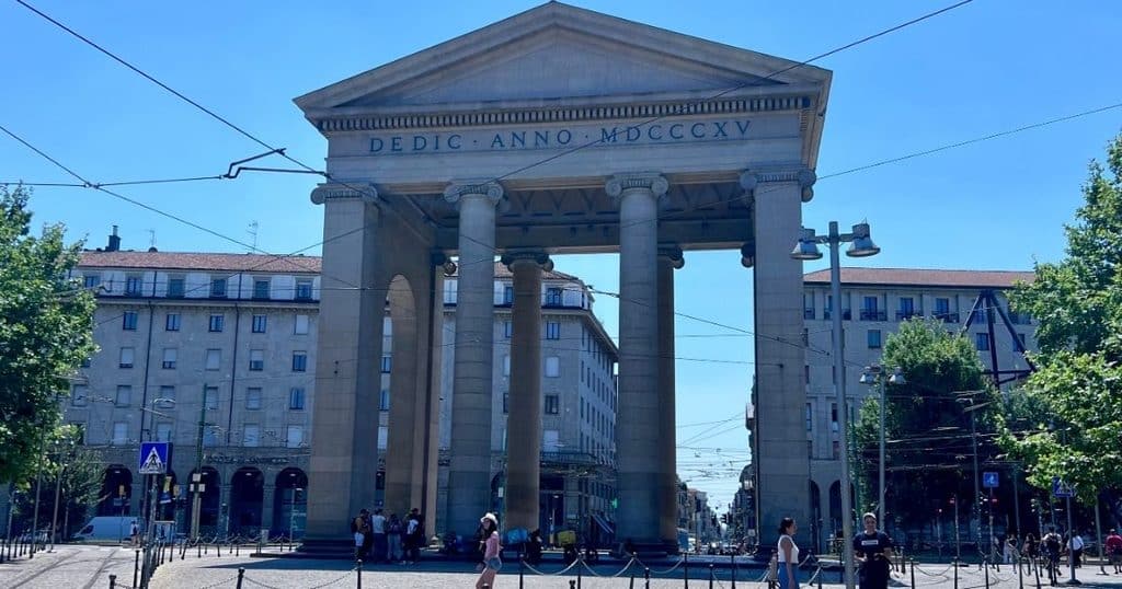 Secret Food Tour Milan crosses the Arco di Porta Ticinese, a neoclassical stone archway with tall columns marking the entrance to Milan's Naviglio Grande neighborhood