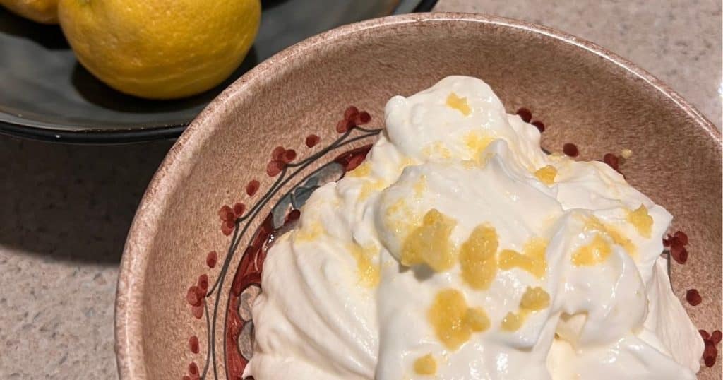 Lemon mousse with lemon zest on top in a bowl and lemons on the side.
