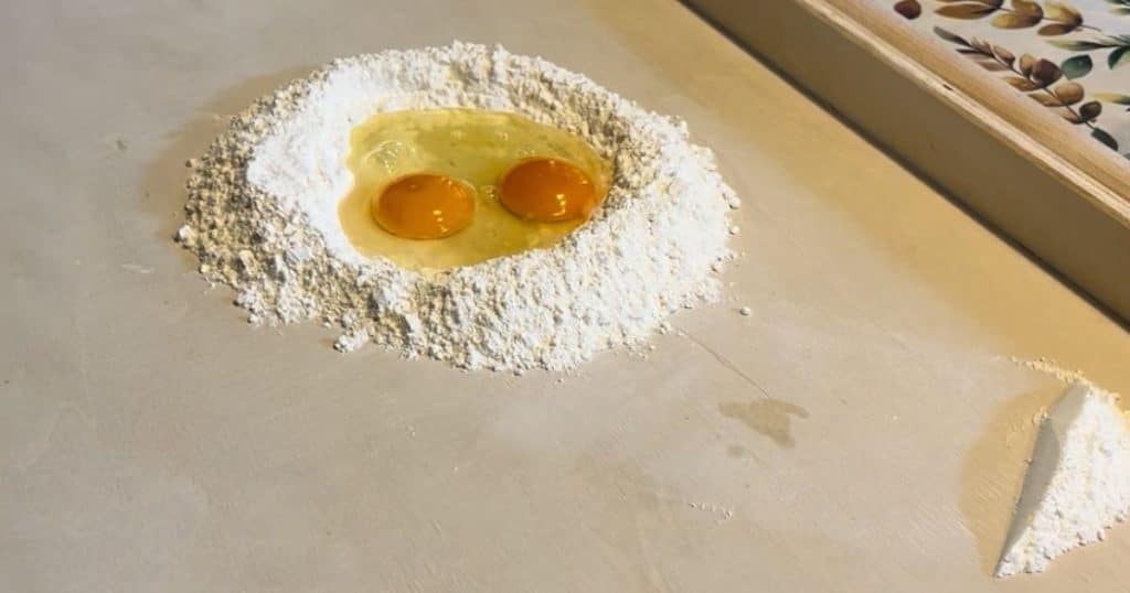 A mound of white flour with two egg yolks in the center for making fresh pasta.